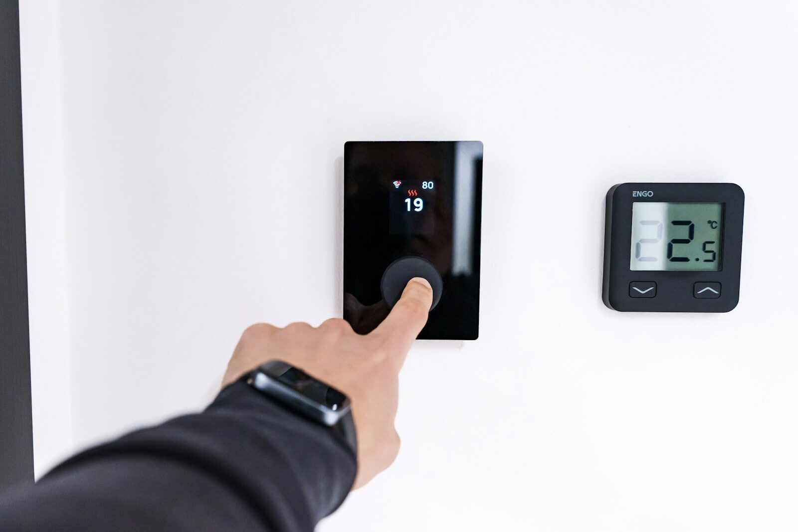 Doigt appuyant sur un thermostat connecté mural